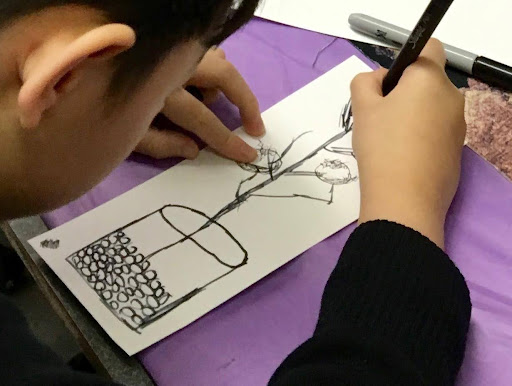 Child draws with a black pen, what looks like a plant in a jar with rocks at the bottom.